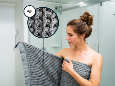 Magnified artistic rendering of silver ions eliminating musty smells on Silverthread Towel being worn by a woman.